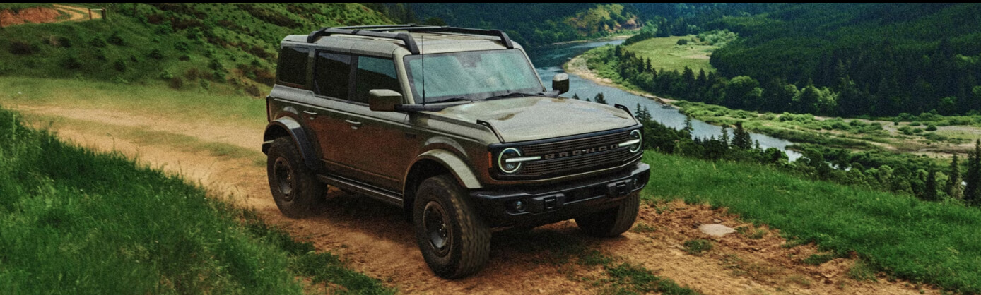 A green Ford Bronco drives down a forest road.