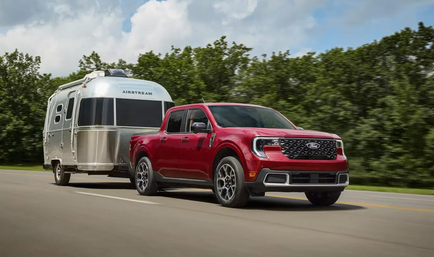 Front three-quarter view of red Ford Maverick Lariat towing an Airstream trailer on a highway.