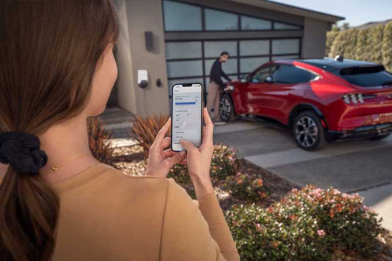 A woman on her phone with a man charging his Mustang Mach-E in the driveway