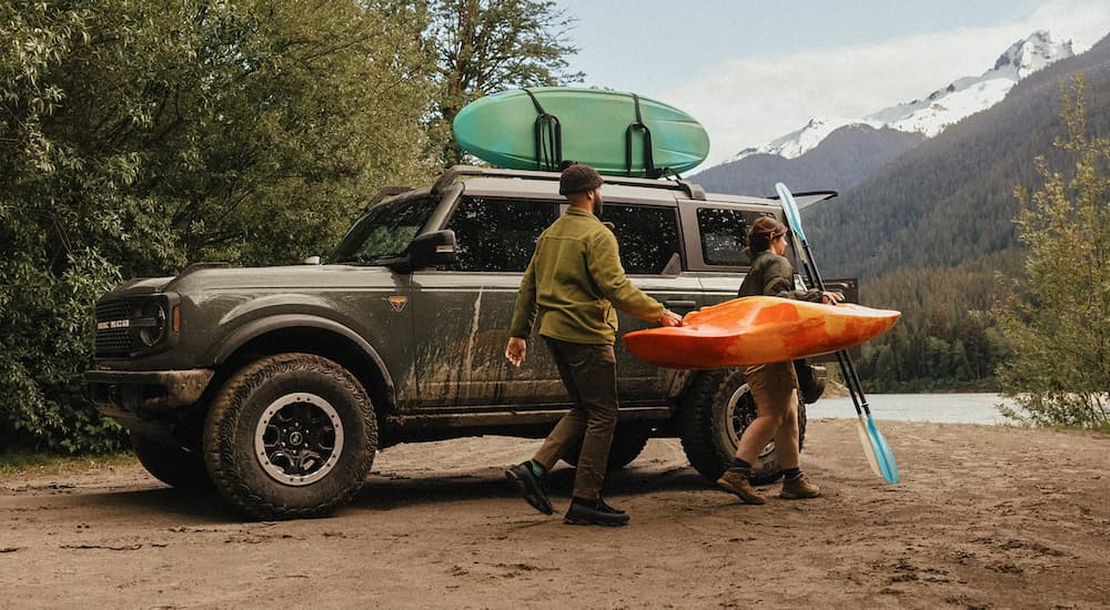 Two people carrying a kayak next to a brown 2026 Ford Bronco