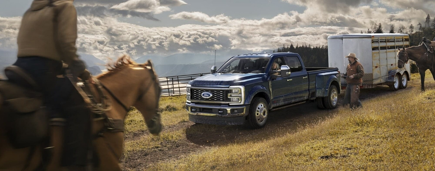 A blue 2023 used Ford F-450 for sale towing a trailer.