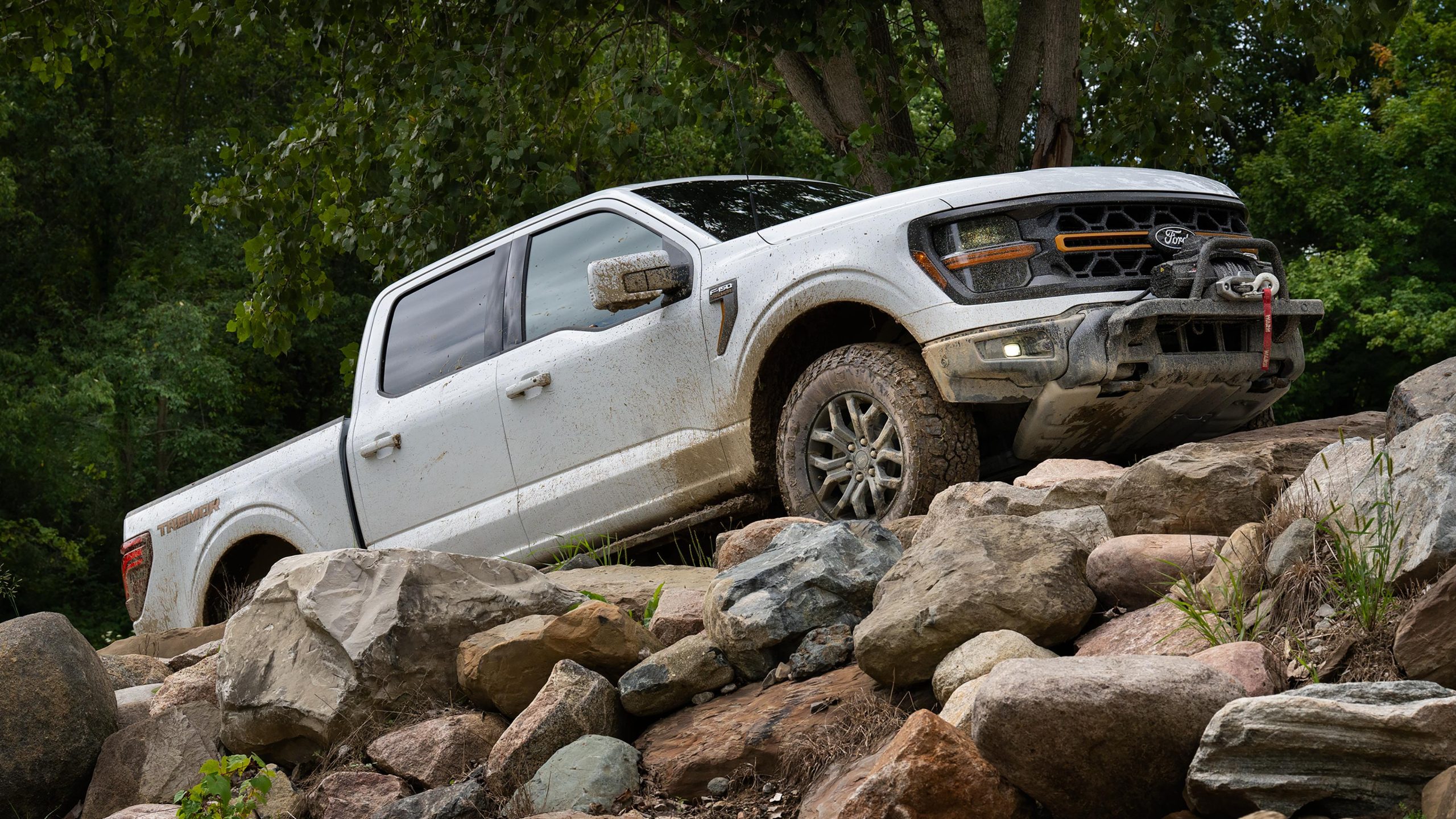 A white Ford F-150 driving up a rocky path with dirt on it.