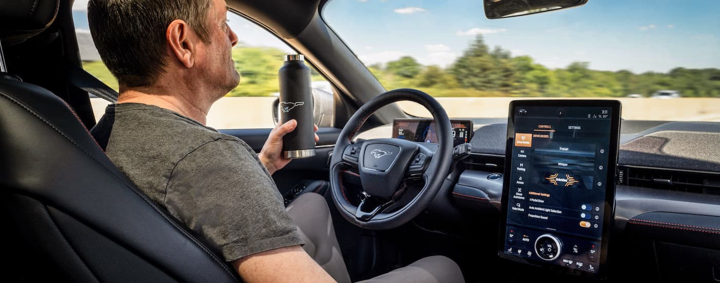 A man is shown holding a water bottle while using the Blue Cruise feature in a 2022 Ford Mustang Mach-E.