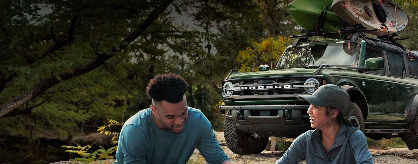 People are shown near a green 2023 Ford Bronco with kayaks on the roof.