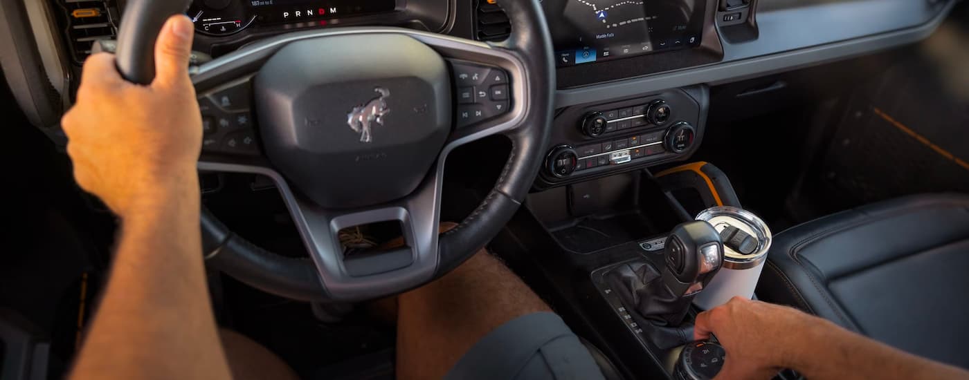 A person is shown steering a 2023 Ford Bronco from the interior.