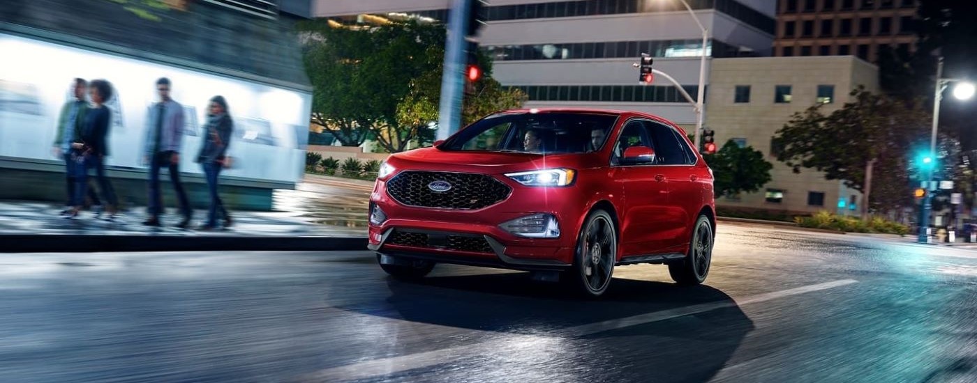 A red 2023 Ford Edge ST is shown driving on a city street at night.