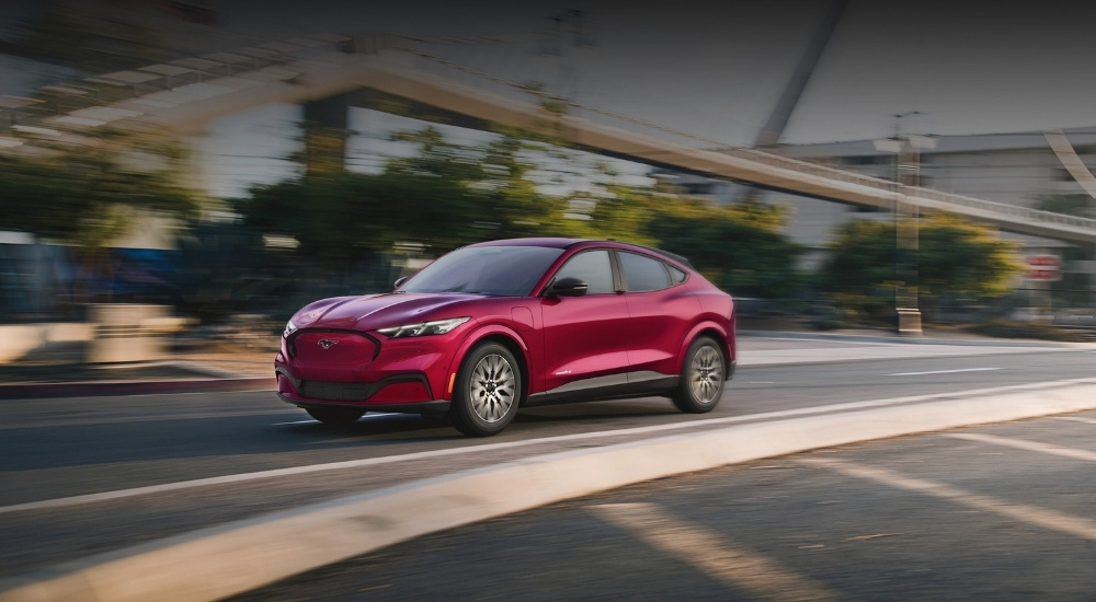A red 2025 Ford Mustang Mach-E driving on a city street.