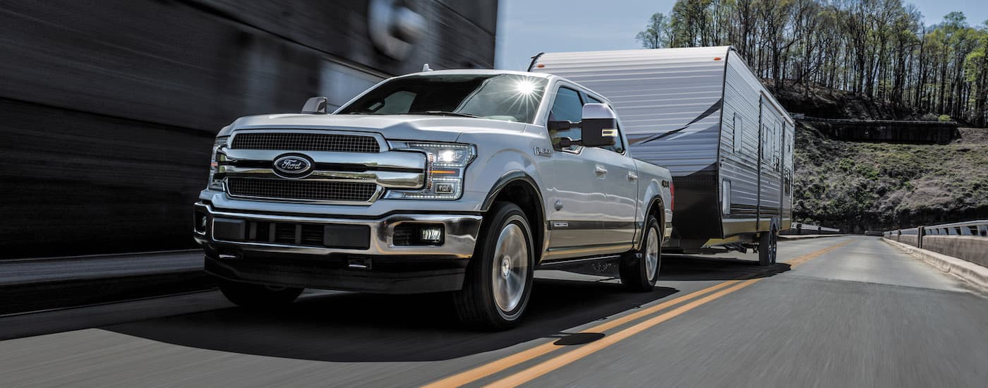 A white 2018 Ford F-150 towing a trailer on an open road.