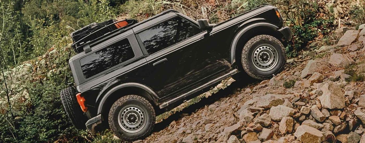 Black 2025 Ford Bronco Base off-roading on a steep dirt trail.