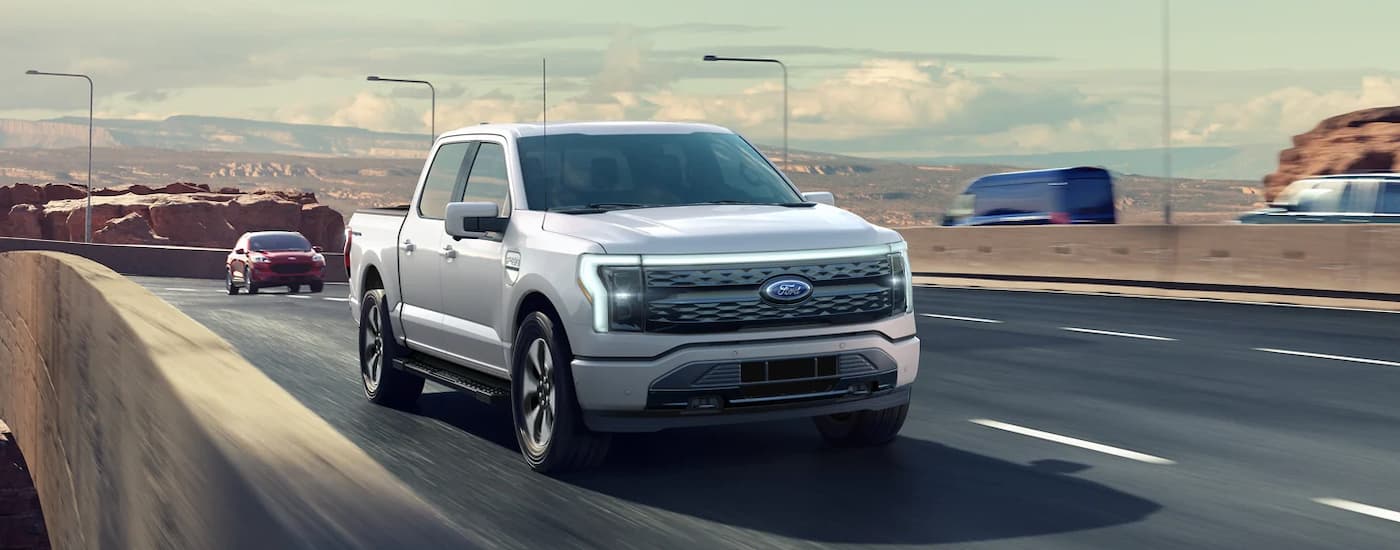 A white 2022 Ford F-150 Lightning pre-order is shown driving on an open highway.