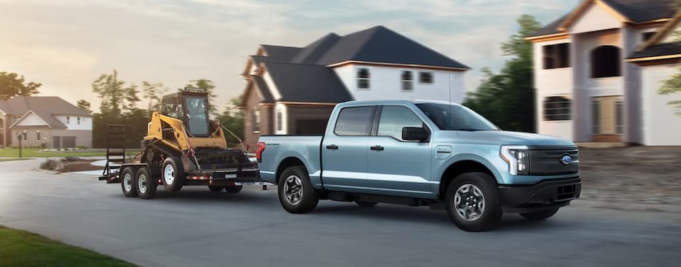 A blue 2022 Ford F-150 Lightning is shown towing heavy machinery.