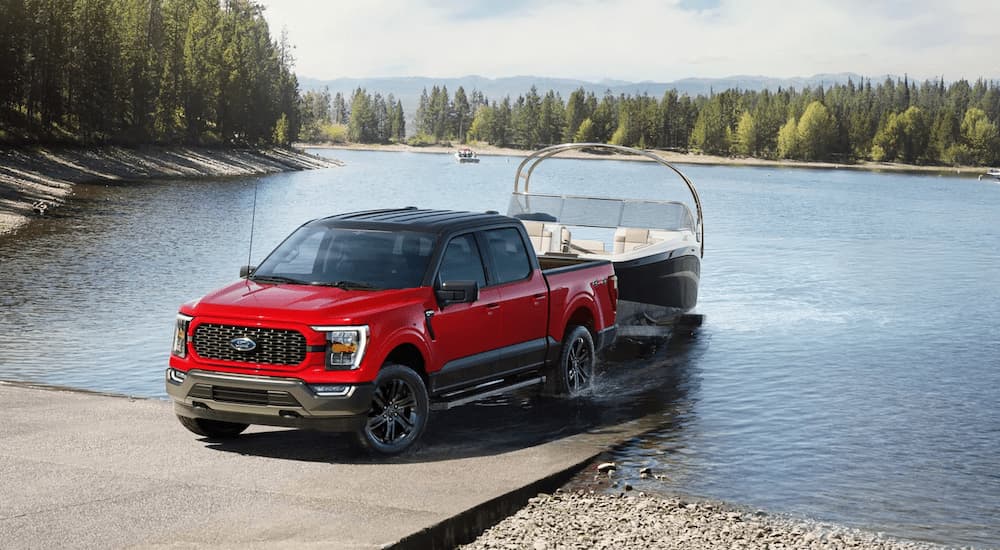 A red 2023 Ford F-150 Heritage Edition towing a boat out of a lake surrounded by trees