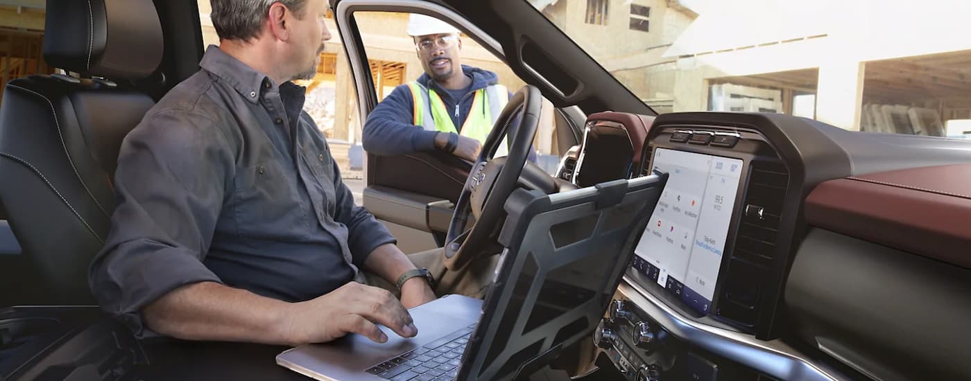 A construction worker is shown using a laptop inside of a 2023 Ford F-150.