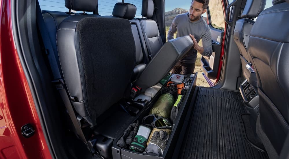 Man getting tools from the rear seat storage in a red 2025 Ford F-150