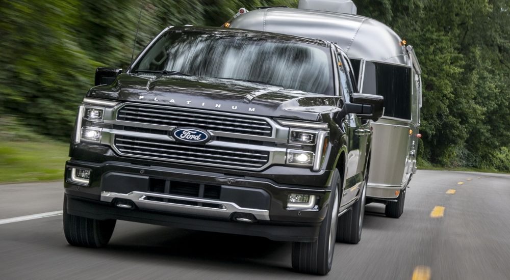 Grey 2025 Ford F-150 towing a silver trailer on a tree-lined road