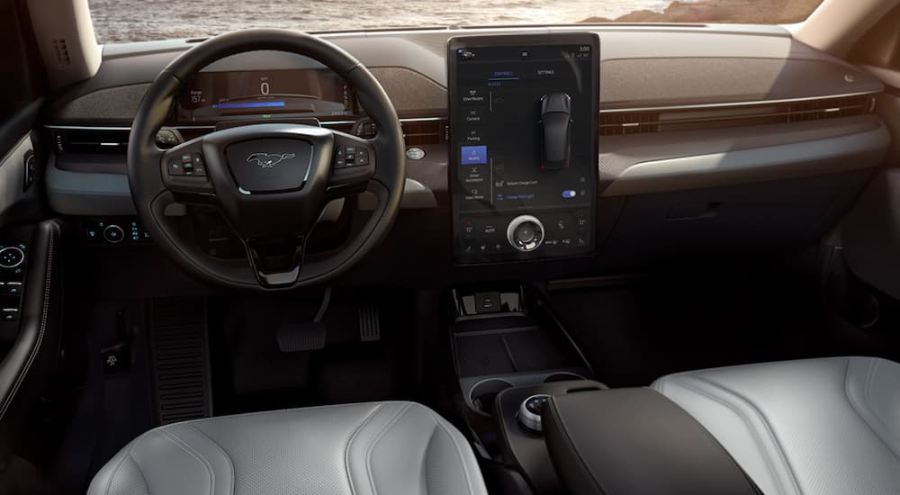 The grey interior of a 2022 Ford Mustang Mach-E shows the steering wheel and infotainment screen.