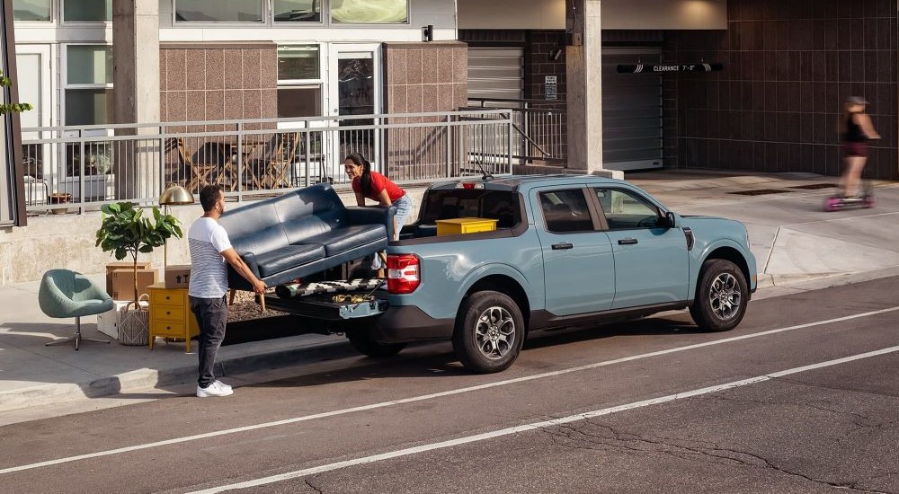 A blue 2023 Ford Maverick is shown on a city street being loaded with a couch.