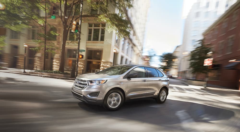 A silver 2018 Ford Edge is shown driving though a city intersection.