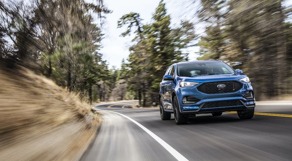 A blue 2019 Ford Edge ST is shown driving on a wooded road after leaving a Sacramento Certified Pre-Owned Ford dealer.