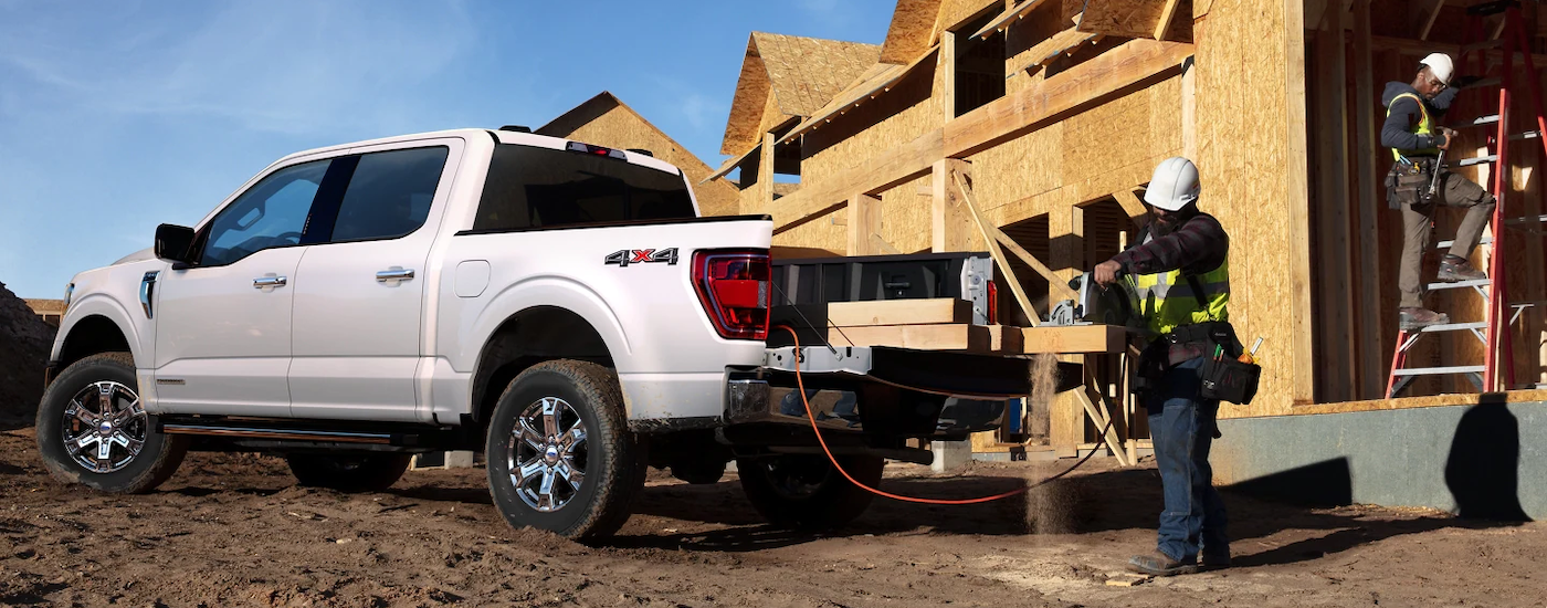 A contractor using the tailgate of a white 2022 Ford F-150 at a residential construction site