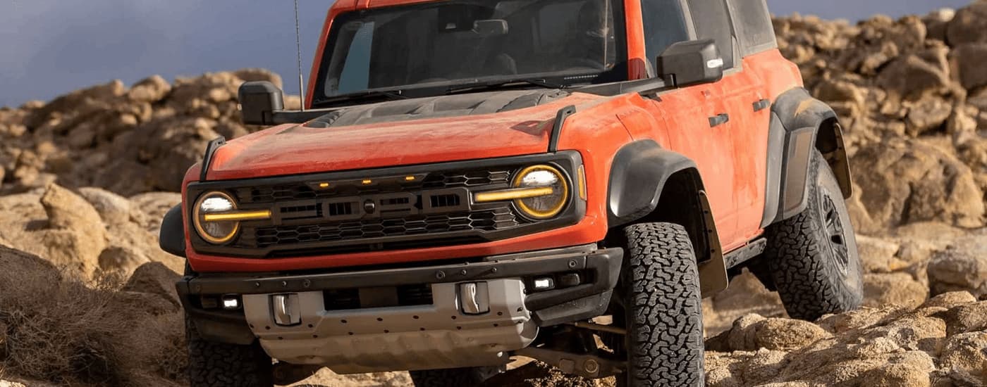 A close up of an orange 2022 Ford Bronco Raptor is shown traversing over a rocky trail.