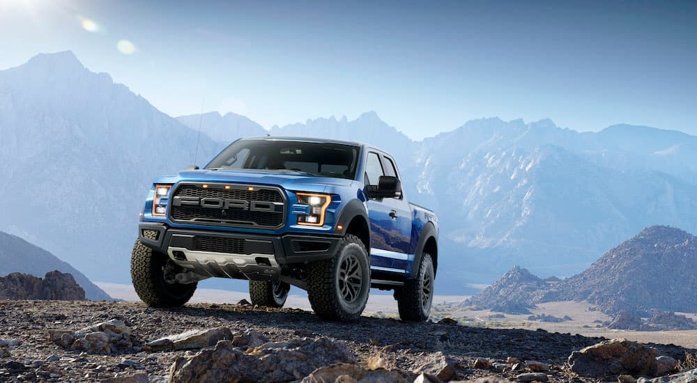 A blue 2017 Ford F-150 Raptor parked on an incline in rocky mountain terrain