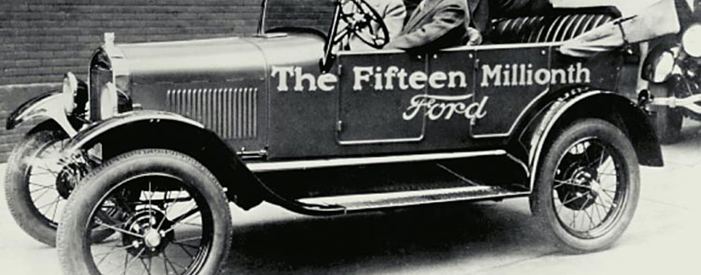 A black and white photo of the fifteen millionth Ford Model T driving in a parade.