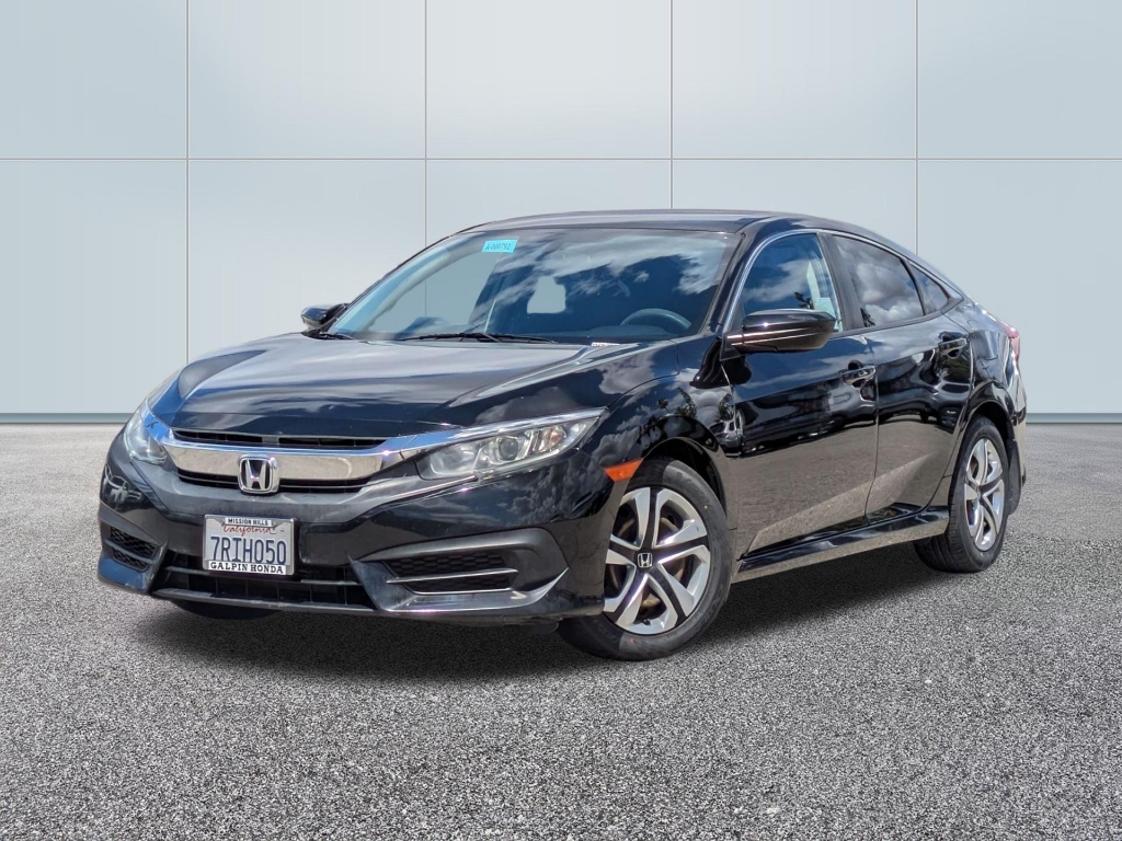 A three-quarter front view of a black Honda Civic sedan (tenth generation, circa 2016–2018) parked on a grey textured surface against a clean, white paneled wall. The vehicle's notable features include: Front Design: A thick chrome "wing" grille bar that spans the width of the front, housing the Honda logo and connecting the sleek headlights. Wheels: Distinctive five-spoke two-tone machined alloy wheels with black inserts. Body Style: A fastback-style roofline characteristic of the tenth-generation Civic sedan. Identification: A California license plate reading "7RIH050" with a "Galpin Honda" dealer frame from Mission Hills. The car's glossy black paint reflects the bright overhead lighting and the blue sky visible in the windshield's reflection.