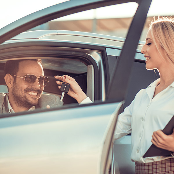 a costumer inside a car with open door receiving the vehicle keys from a sales woman