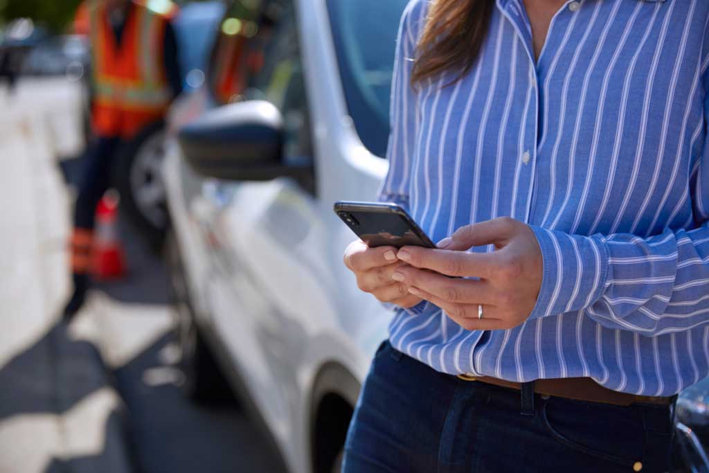 Woman leaning against her car while checking her phone.