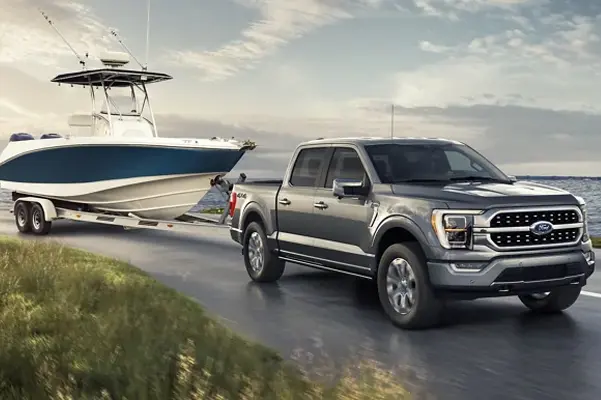 A 2022 Ford F-150 towing a boat on a road next to a lake